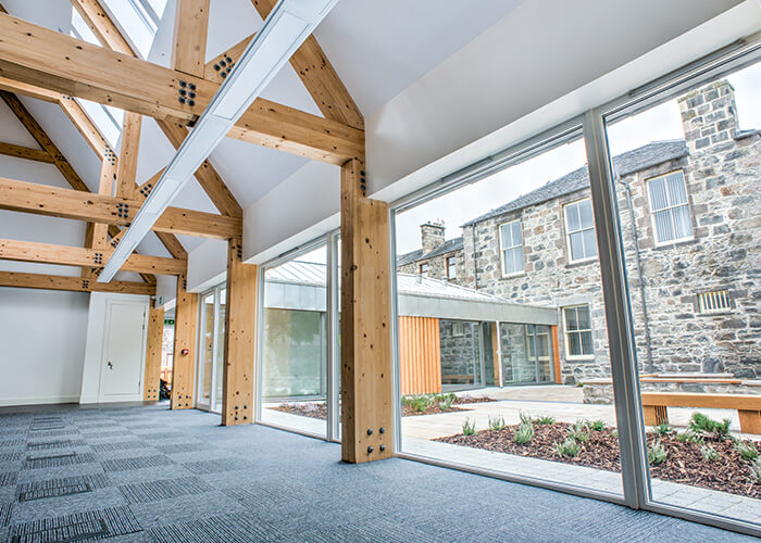 View looking out at Kingussie Courthouse court-yard from within room with large wooden beams and windows.